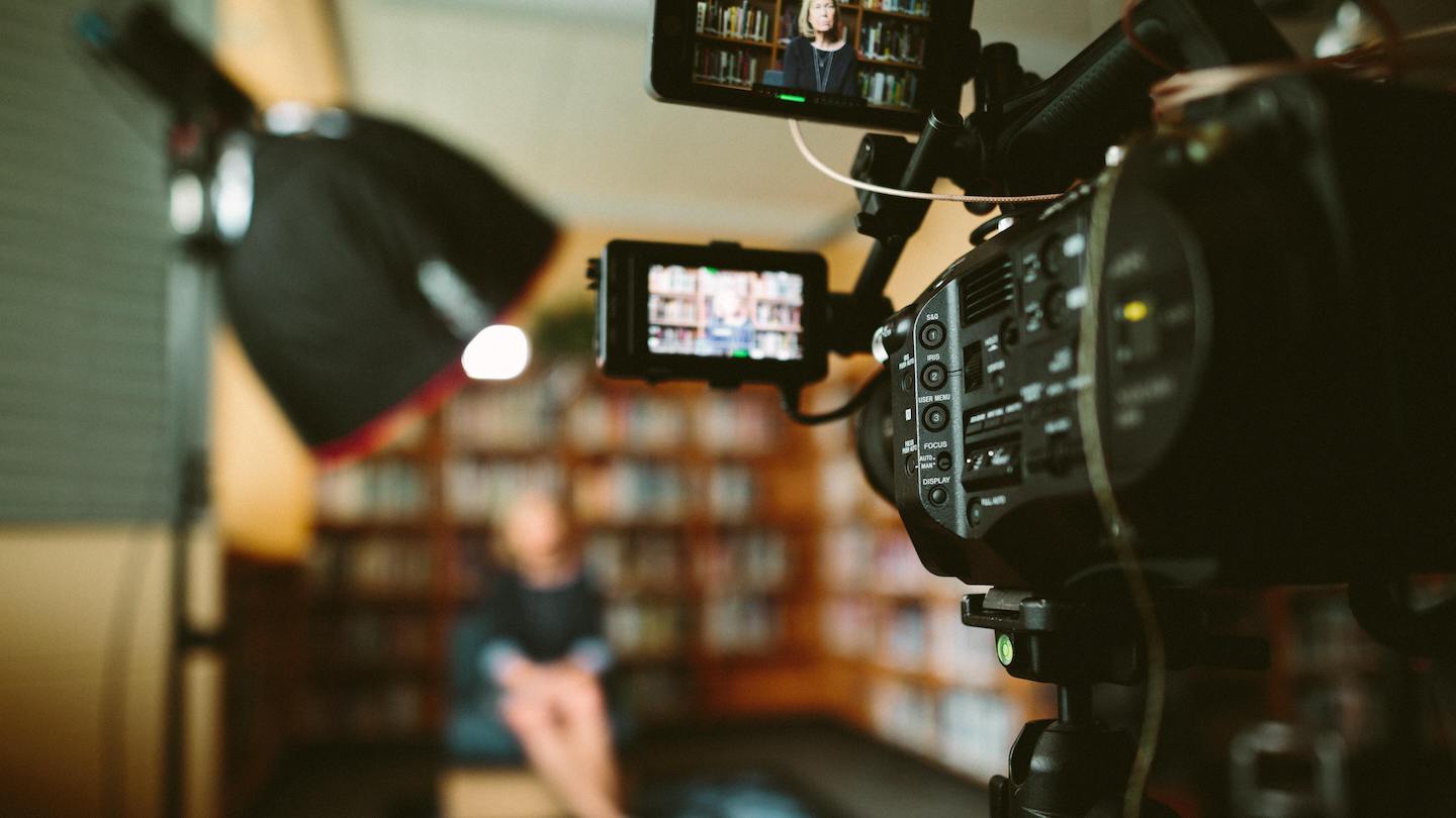 Behind the scenes of a video shoot, camera and light with a blurred background of a lady in a chair