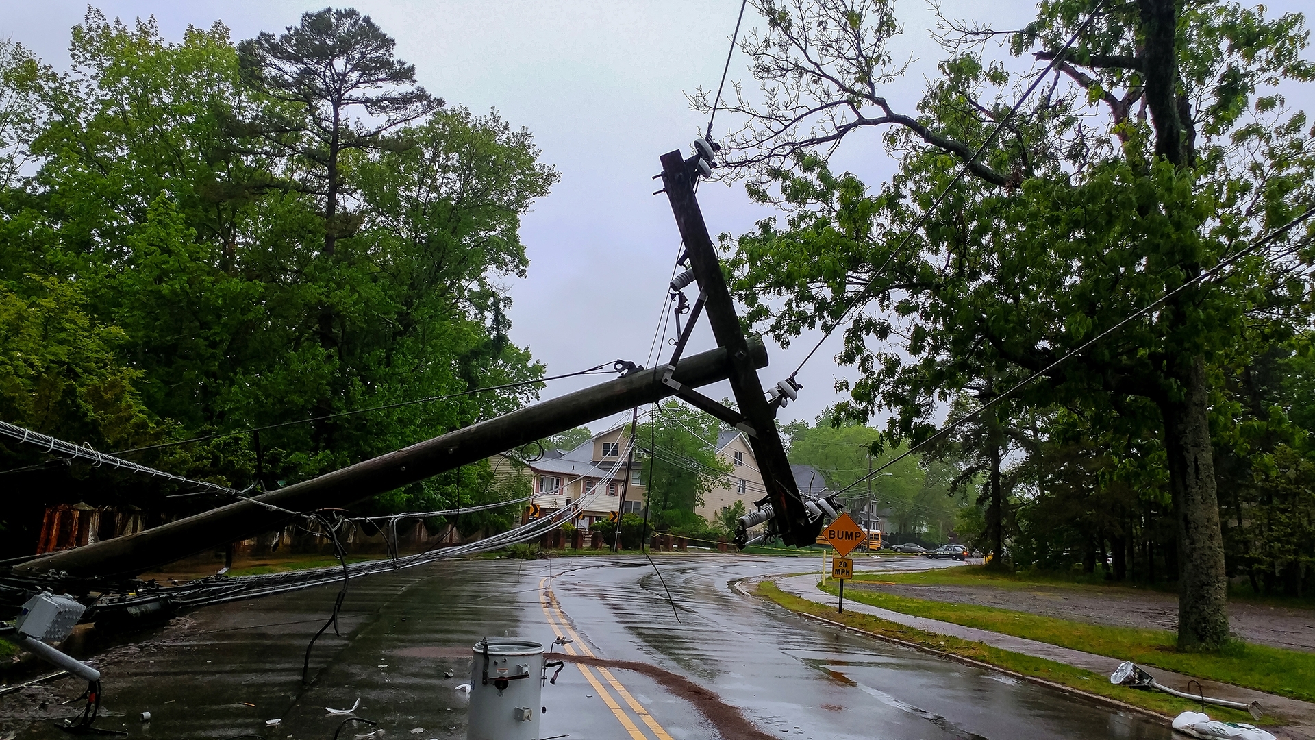 An image of a wet road with a telephone pole down from a storm.